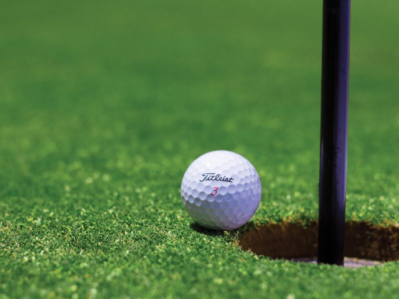 A golf ball sitting on the edge of the hole